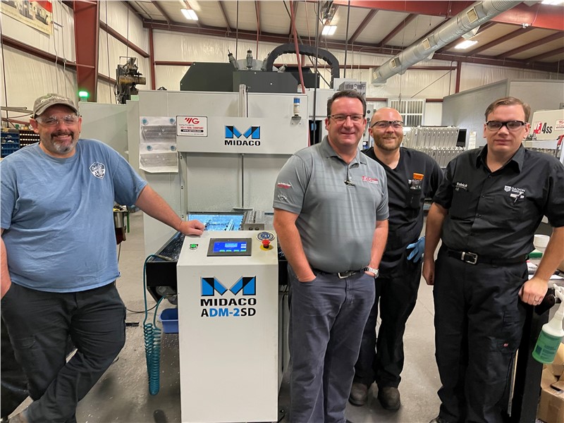Four men standing around a Midaco Pallet Changer System in machine shop