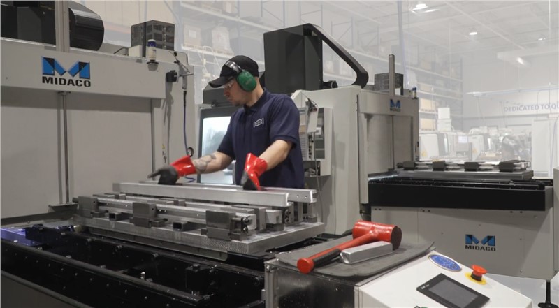 Machinist Loading Parts onto Midaco Pallet Changer with Automatic Pallet Changer in Background