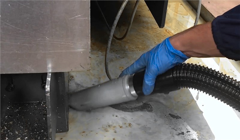 Machinist hand using CNC industrial vacuum nozzle to clean machine
