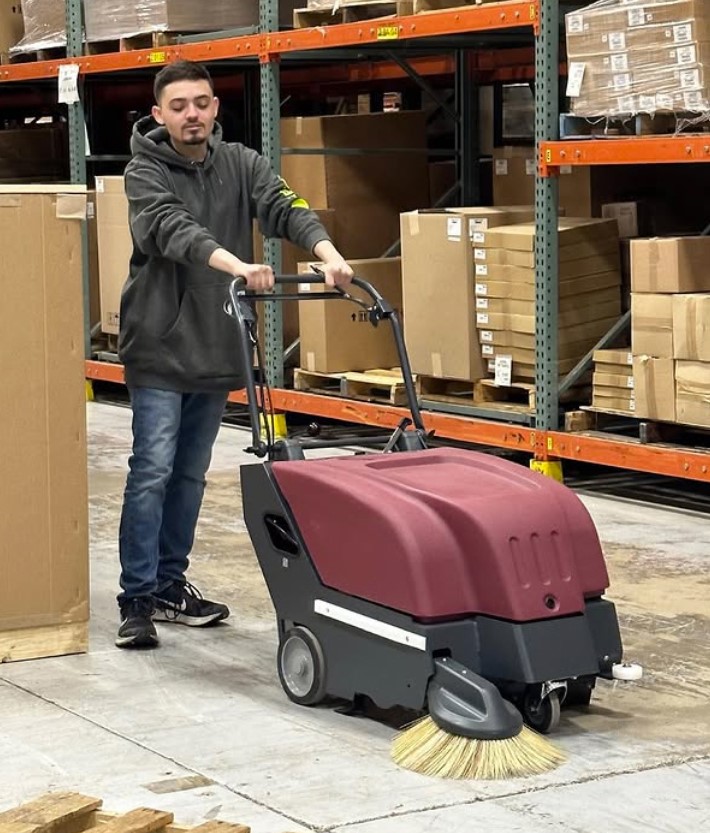 Manu using Midaco Walk Behind Floor Sweeper in warehouse