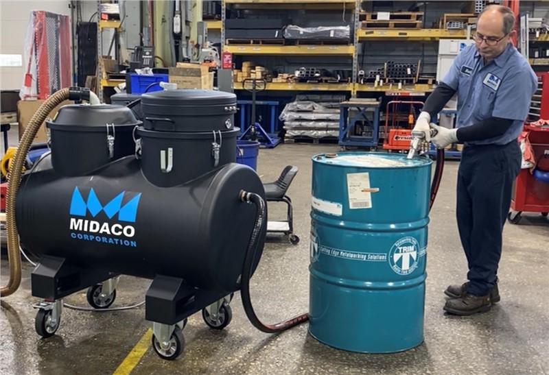 Machinist removing CNC liquid from industrial vacuum into disposal drum